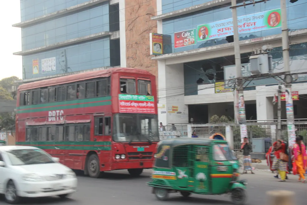 Red city bus and green auto-rickshaw on a Dhaka avenue